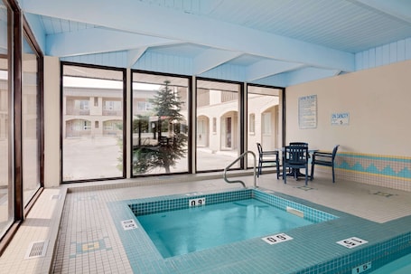 An indoor swimming pool with clear pool depth markers, a seating area with chairs, and large windows offering a view of the outside.