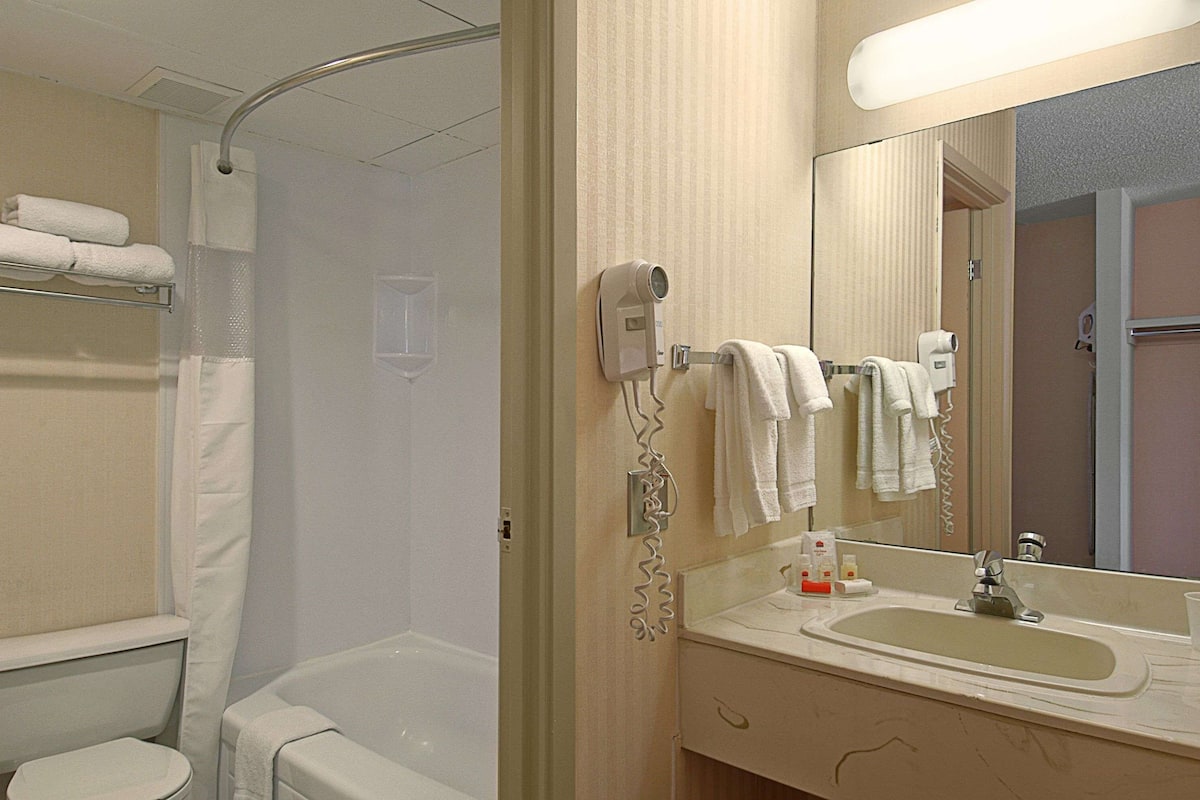 A bathroom with a bathtub, a sink, and a mirror. There are towels hanging on the wall and a hairdryer on the counter.