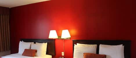 A hotel room with two beds, red walls, and two bedside lamps.
