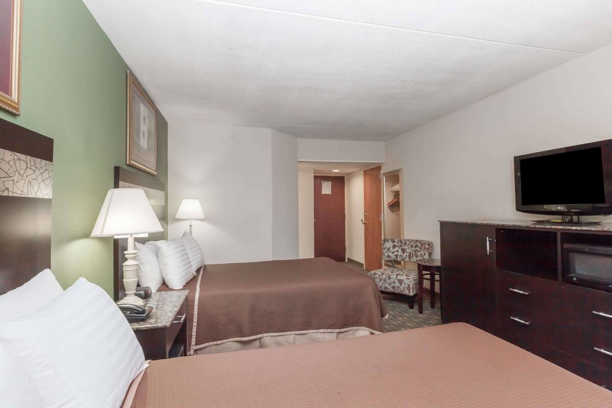 A hotel room with two beds, a television, a desk with a lamp, and a chair.