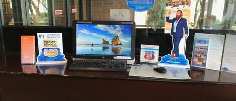 A hotel reception desk with a laptop, a 'Best Travel Rewards' award, a 'Have You Seen?' poster, and a 'Wyndham Rewards' sign.