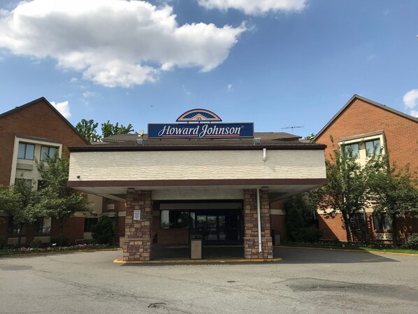 Un motel Howard Johnson con fachada de ladrillo, un cielo azul despejado y un estacionamiento al frente.