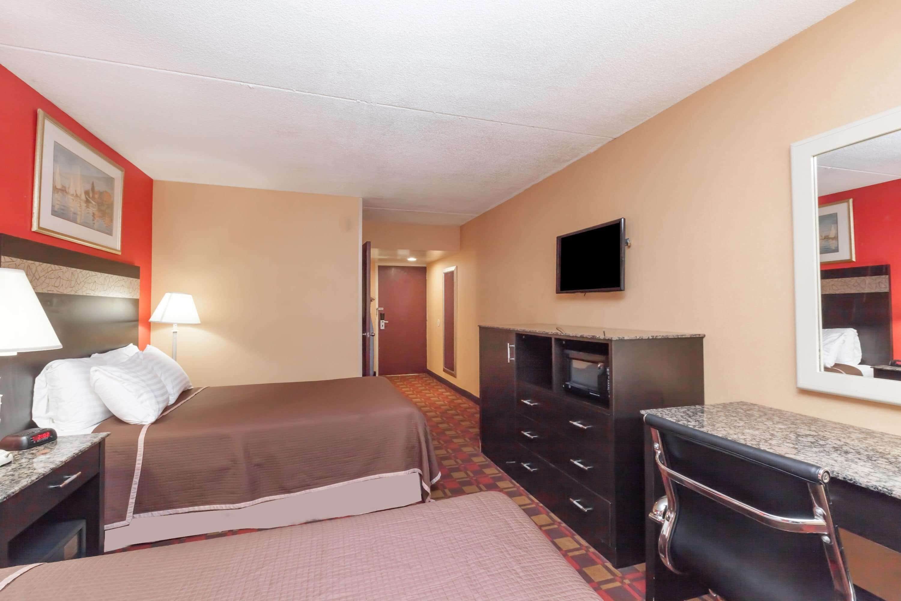 Una habitación de hotel con cama, escritorio con lámpara, cómoda, televisión y espejo.