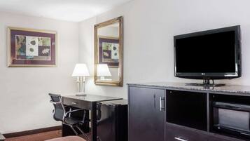 Habitación de hotel con cama, escritorio, silla, televisor, espejo y armario.