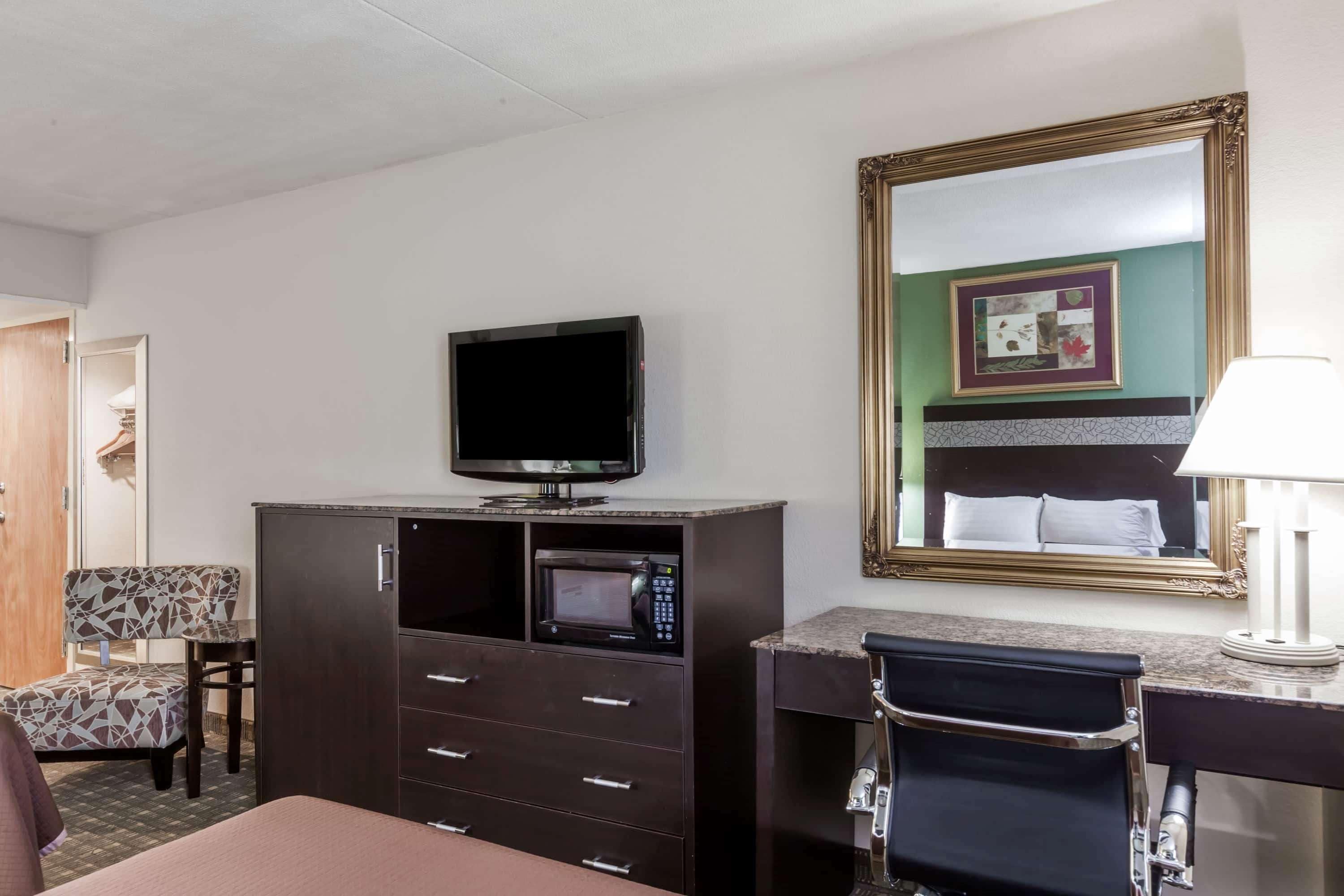 Habitación de hotel con cama, televisión, microondas, escritorio con lámpara, silla y un espejo grande.