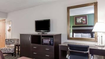 Habitación de hotel con cama, televisión, microondas, escritorio con lámpara, silla y un espejo grande.