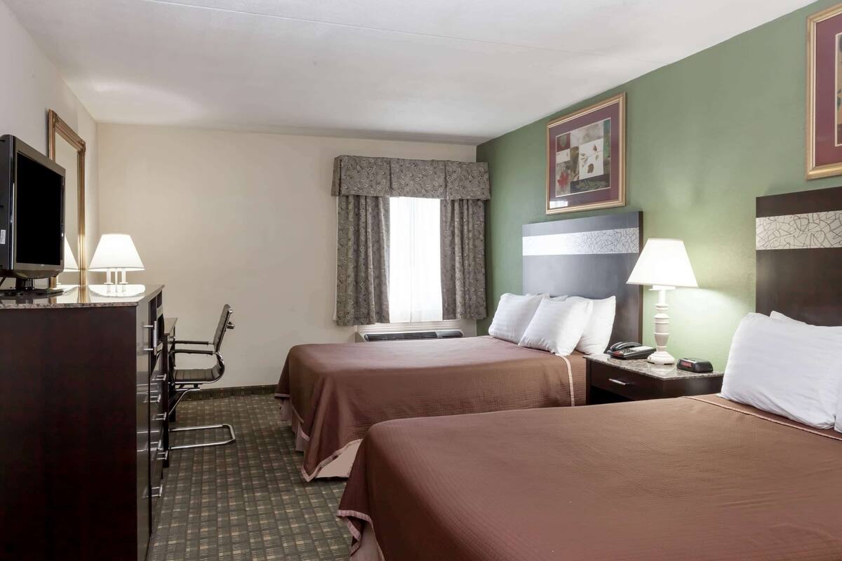A hotel room with two beds, a desk with a lamp, a television, and a chair.