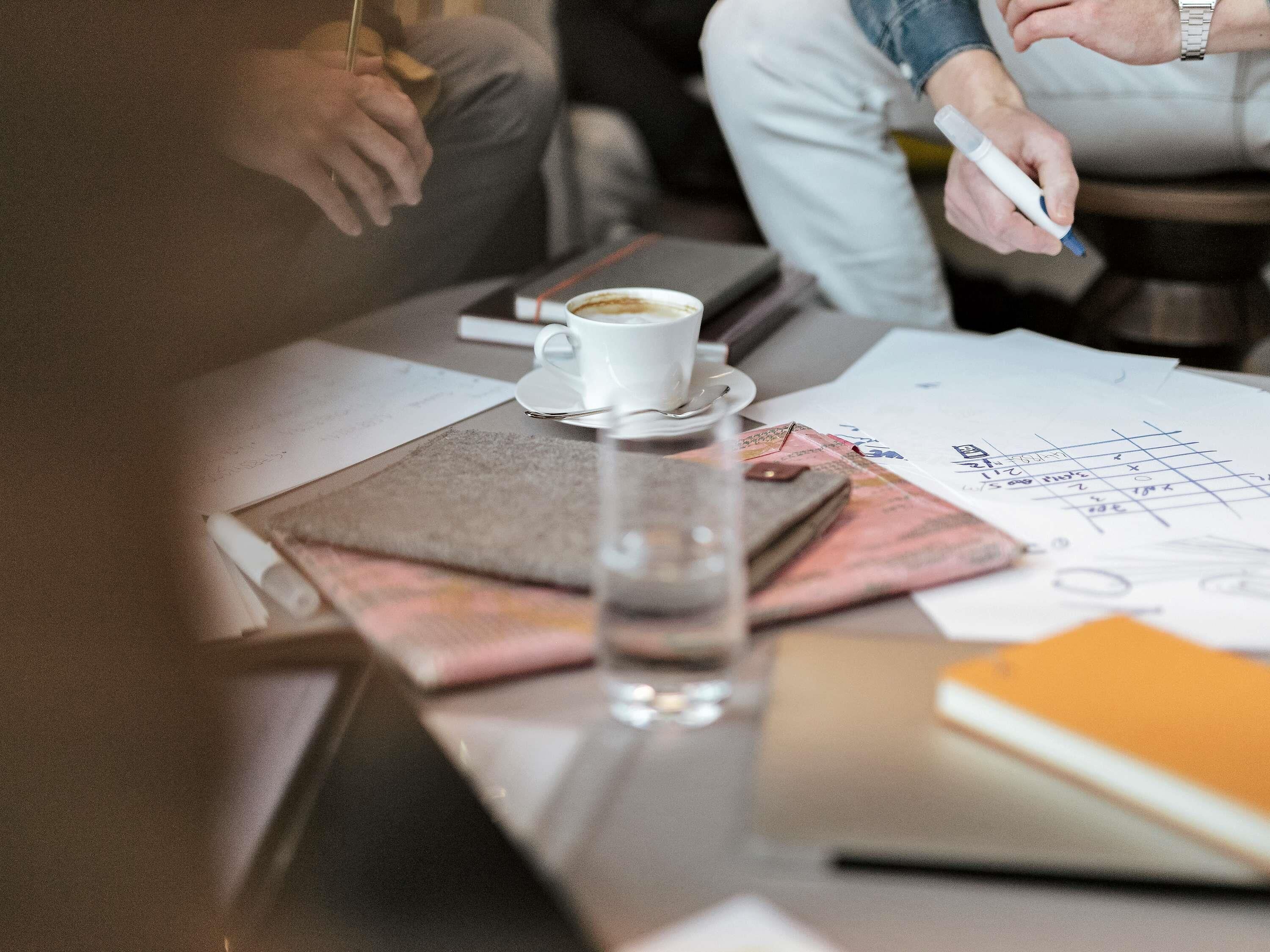 Una mesa con una taza de café, papeles, un cuaderno y un bolígrafo.