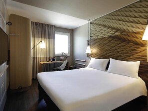 A hotel room with a bed, desk, chair, lamp, and a television. - ibis Porto Gaia (Vila Nova de Gaia)