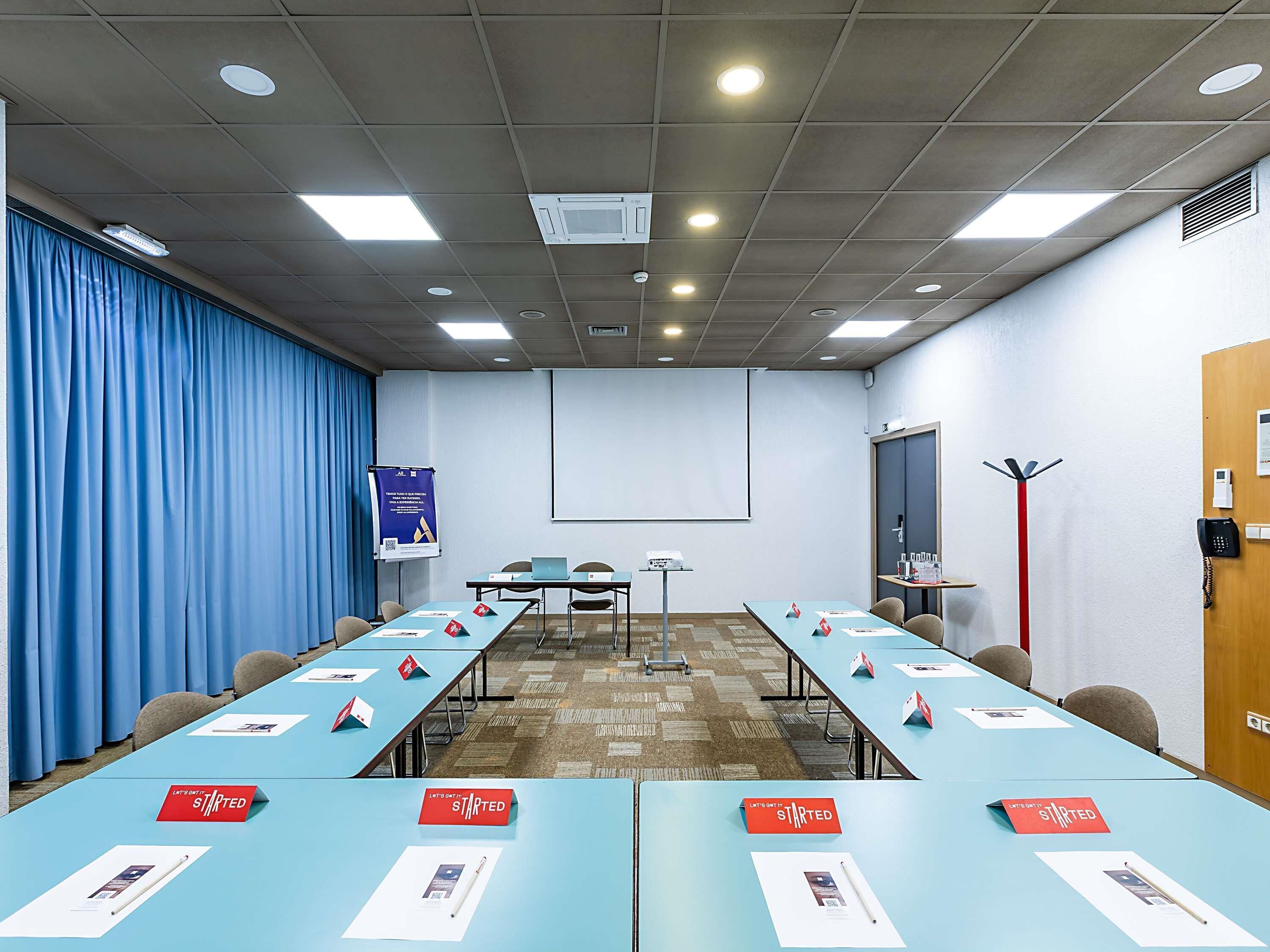 A conference room with a long table, chairs, a projector screen, and a blue curtain.