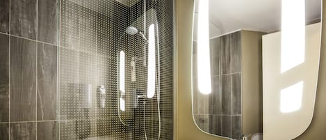 A modern bathroom with a large mirror, a white sink, and a shower area with a glass door.