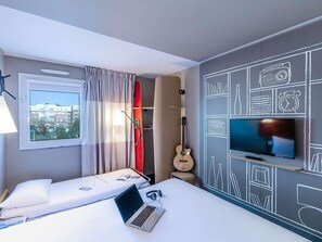 Ein Hotelzimmer mit einem Bett, einem Laptop, einer Gitarre, einem Fernseher und einer Wand mit Kreidezeichnungen.