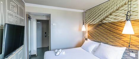 Habitación de hotel con cama, televisión, puerta y pared con diseño texturizado.