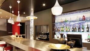 A modern bar area with stainless steel counters, red bar stools, and a variety of liquor bottles displayed on shelves. - ibis Porto Gaia (Vila Nova de Gaia)