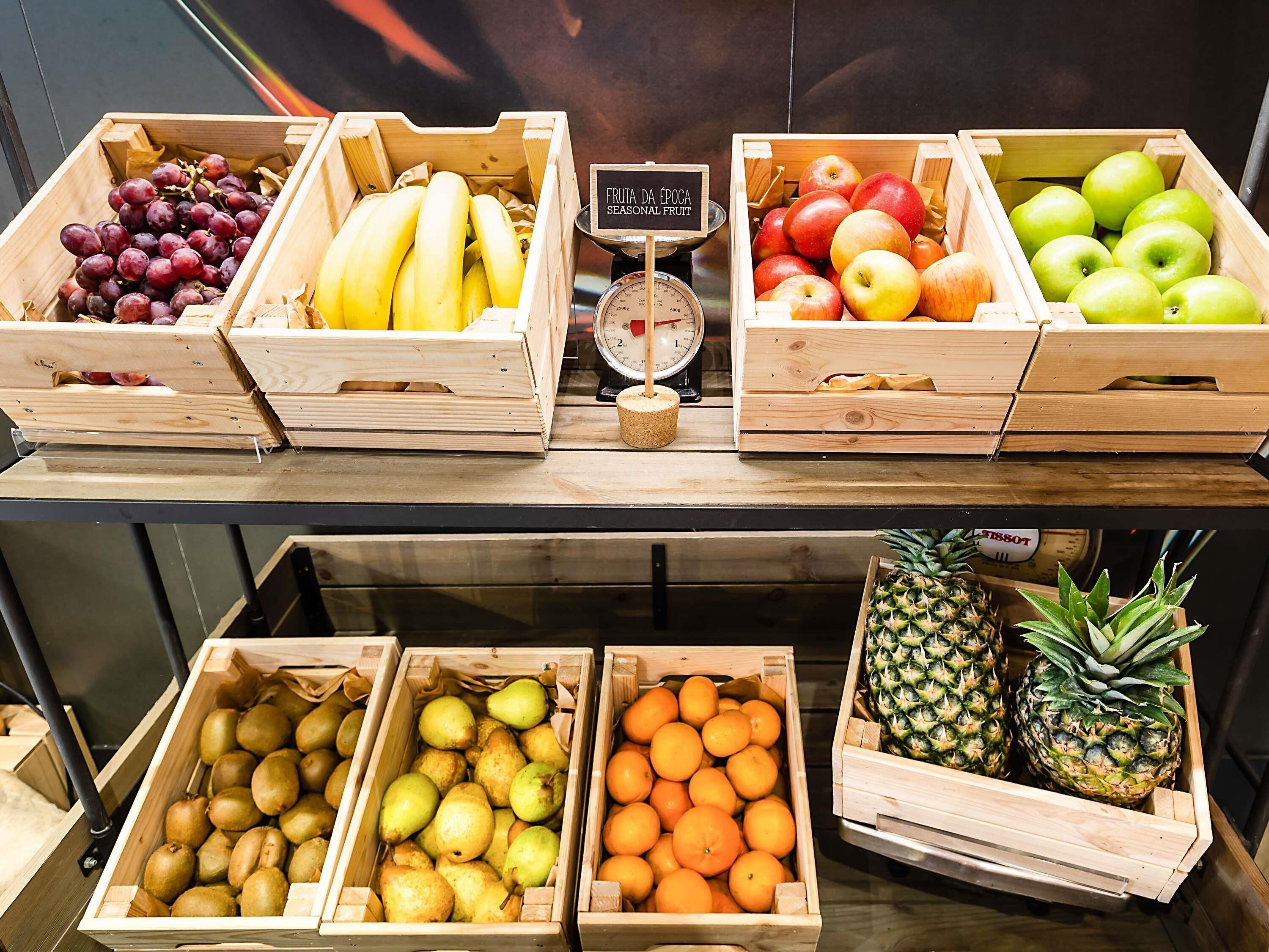 Houten kratten gevuld met diverse soorten fruit en groenten, zoals druiven, bananen, appels, peren, sinaasappels en ananassen.
