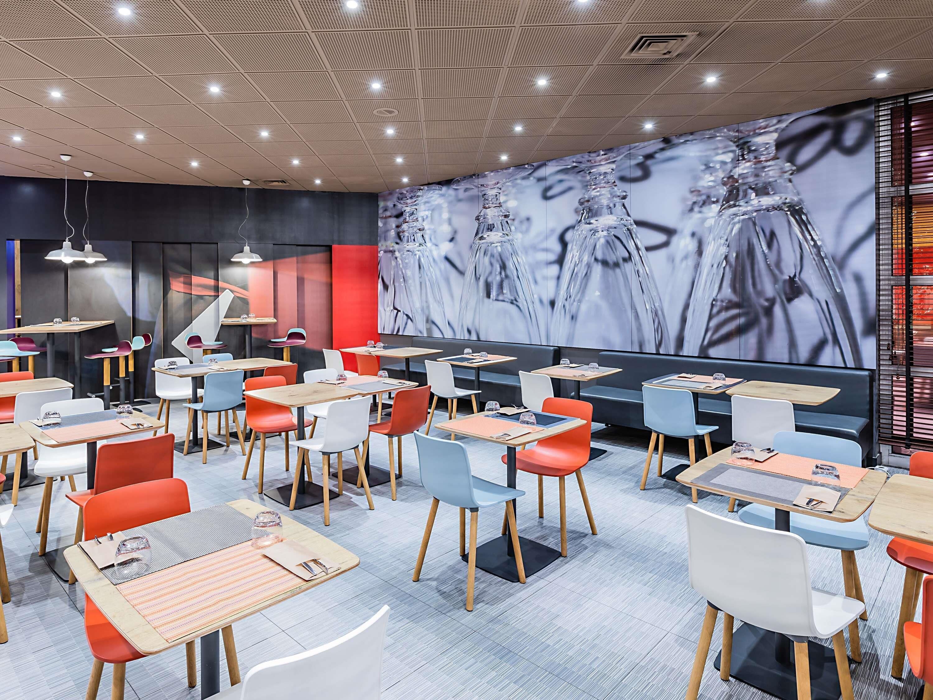 Un restaurante moderno con varias mesas y sillas, una gran pantalla digital mostrando arte abstracto y un techo con diseño.