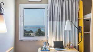 A hotel room with a view of the sea, a table with a laptop, a lamp, and a minibar. - ibis Porto Gaia (Vila Nova de Gaia)