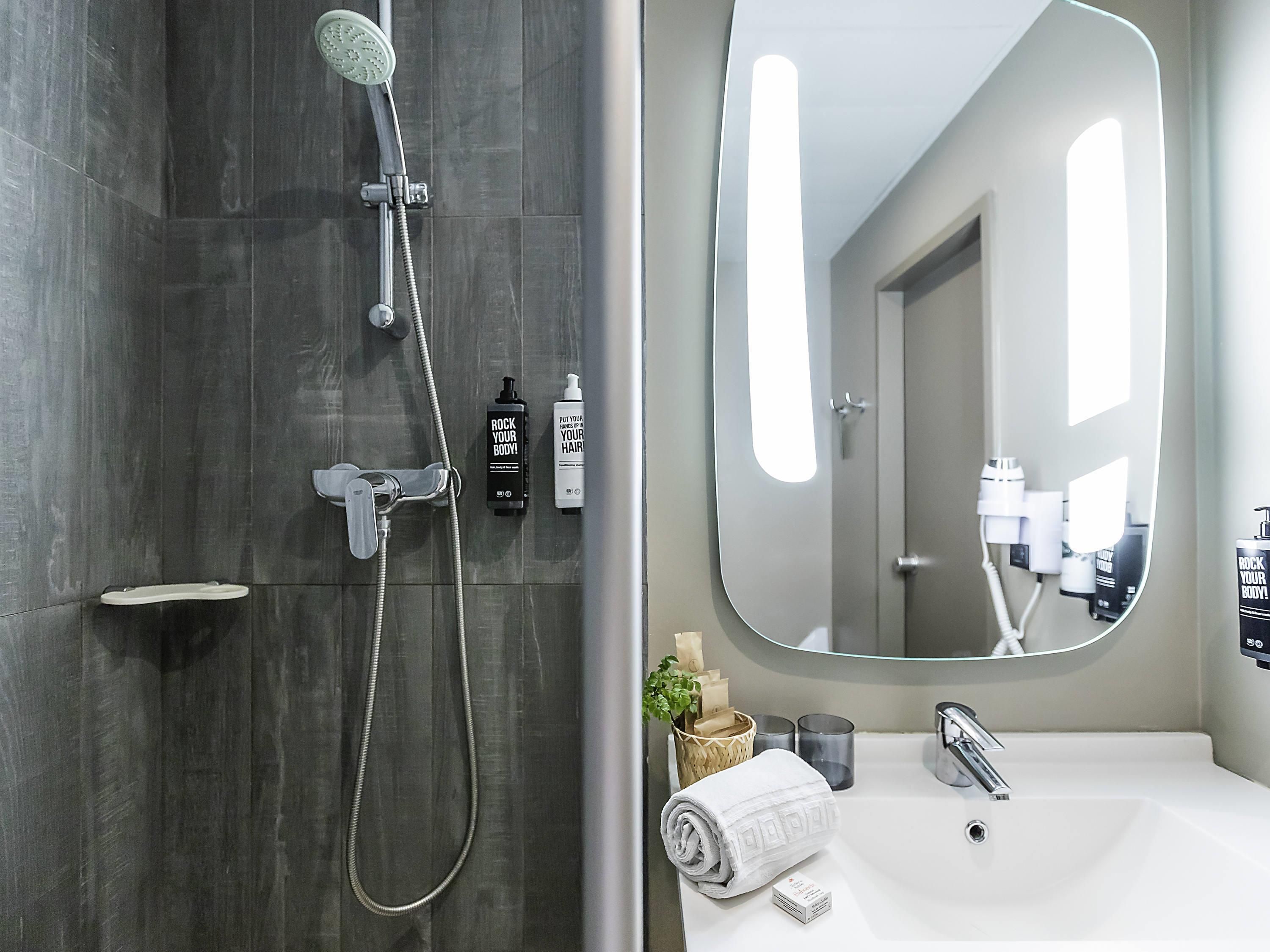 A modern bathroom with a shower, a sink, a mirror, and toiletries.