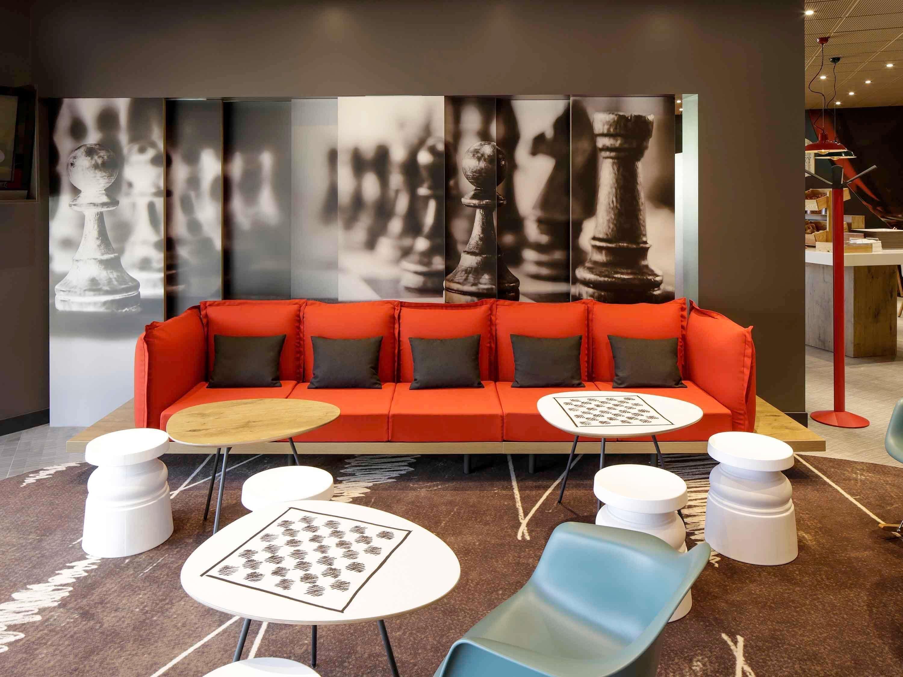 Et moderne loungeområde med en rød sofa, runde hvide borde og et skakbræt-design på et bord.