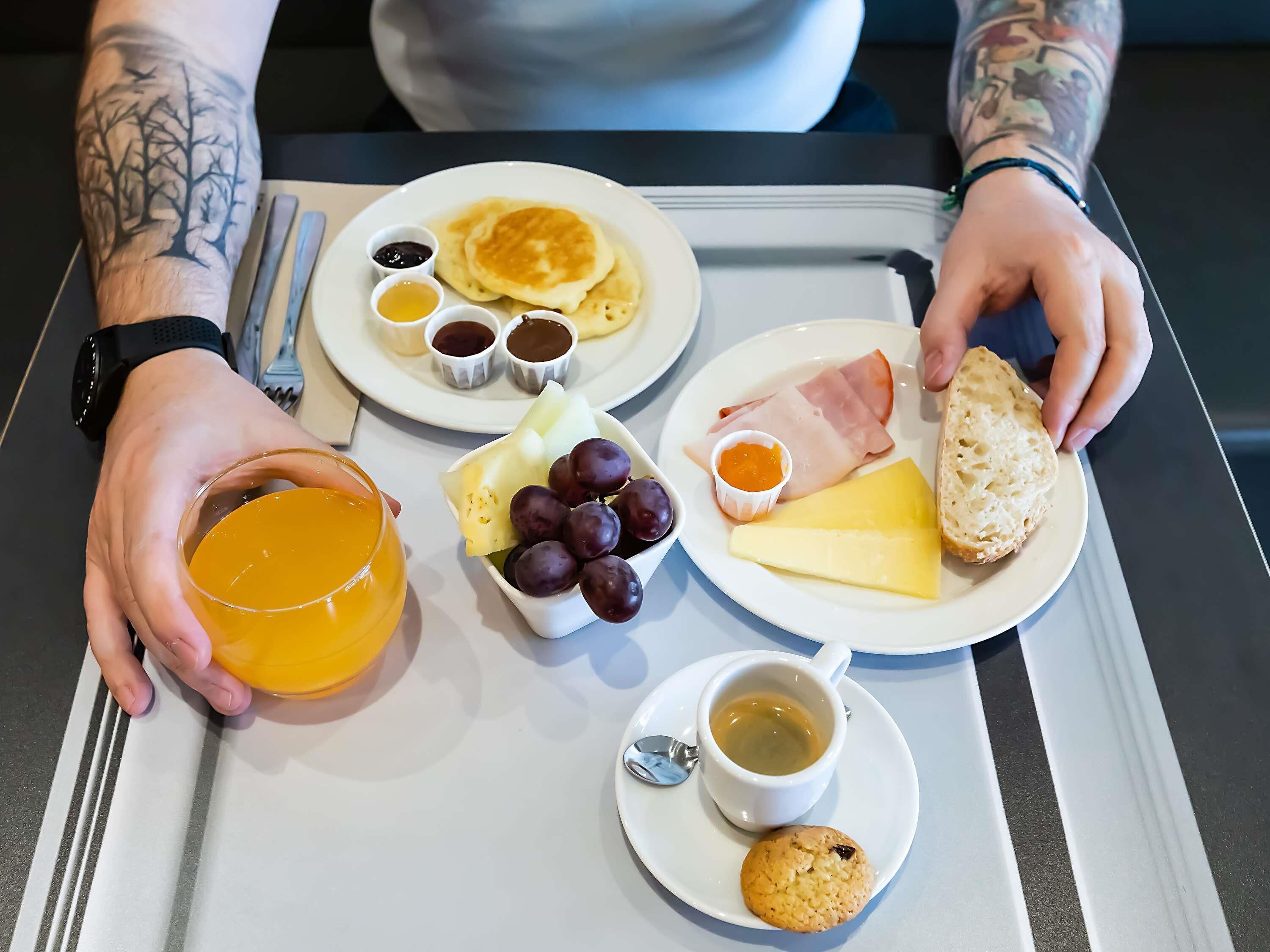 Una bandeja con alimentos para el desayuno, incluyendo panqueques, queso, jamón, pan y un muffin.
