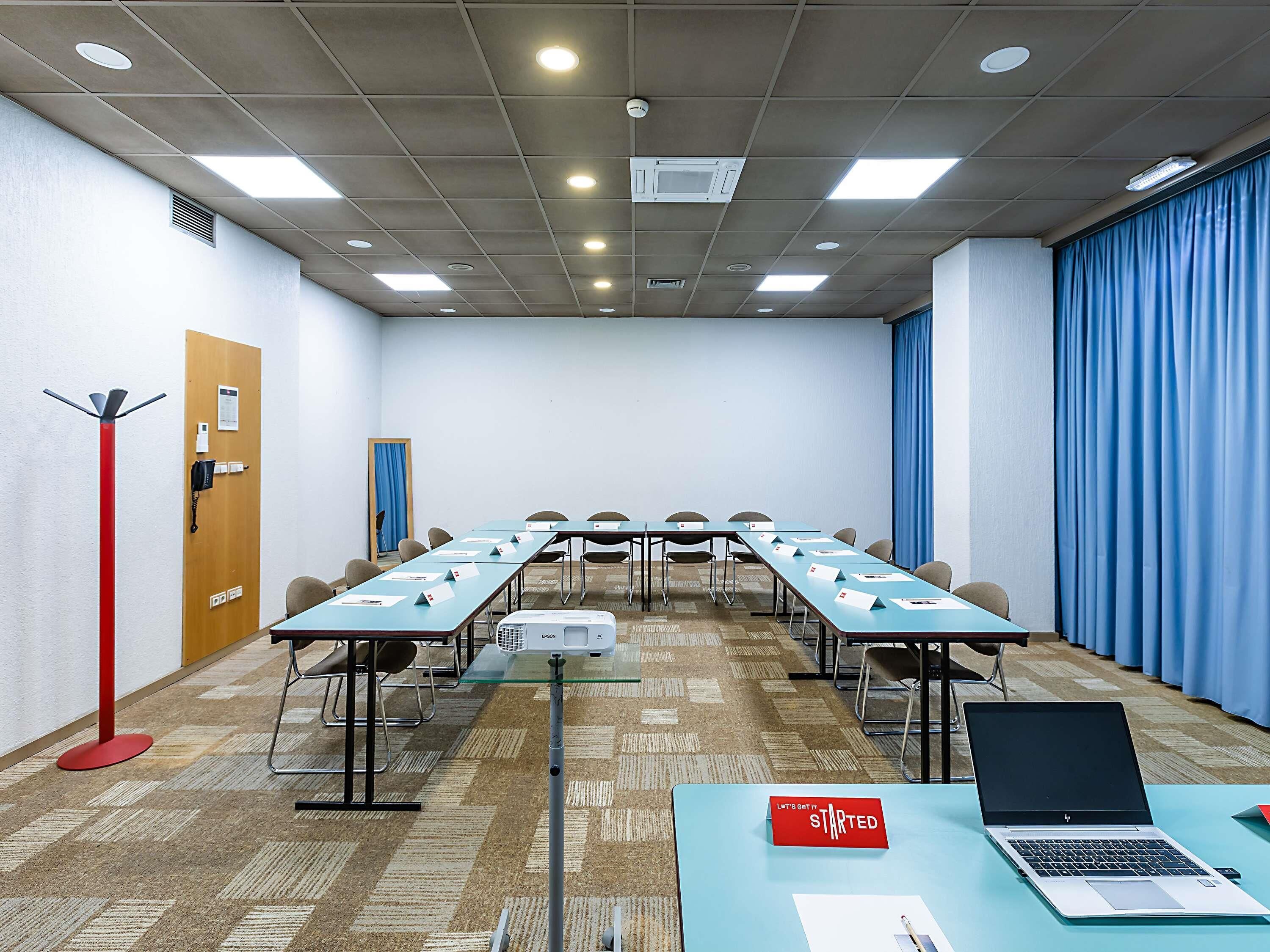 Un salón de conferencias con una larga mesa, sillas, un proyector y una computadora portátil.