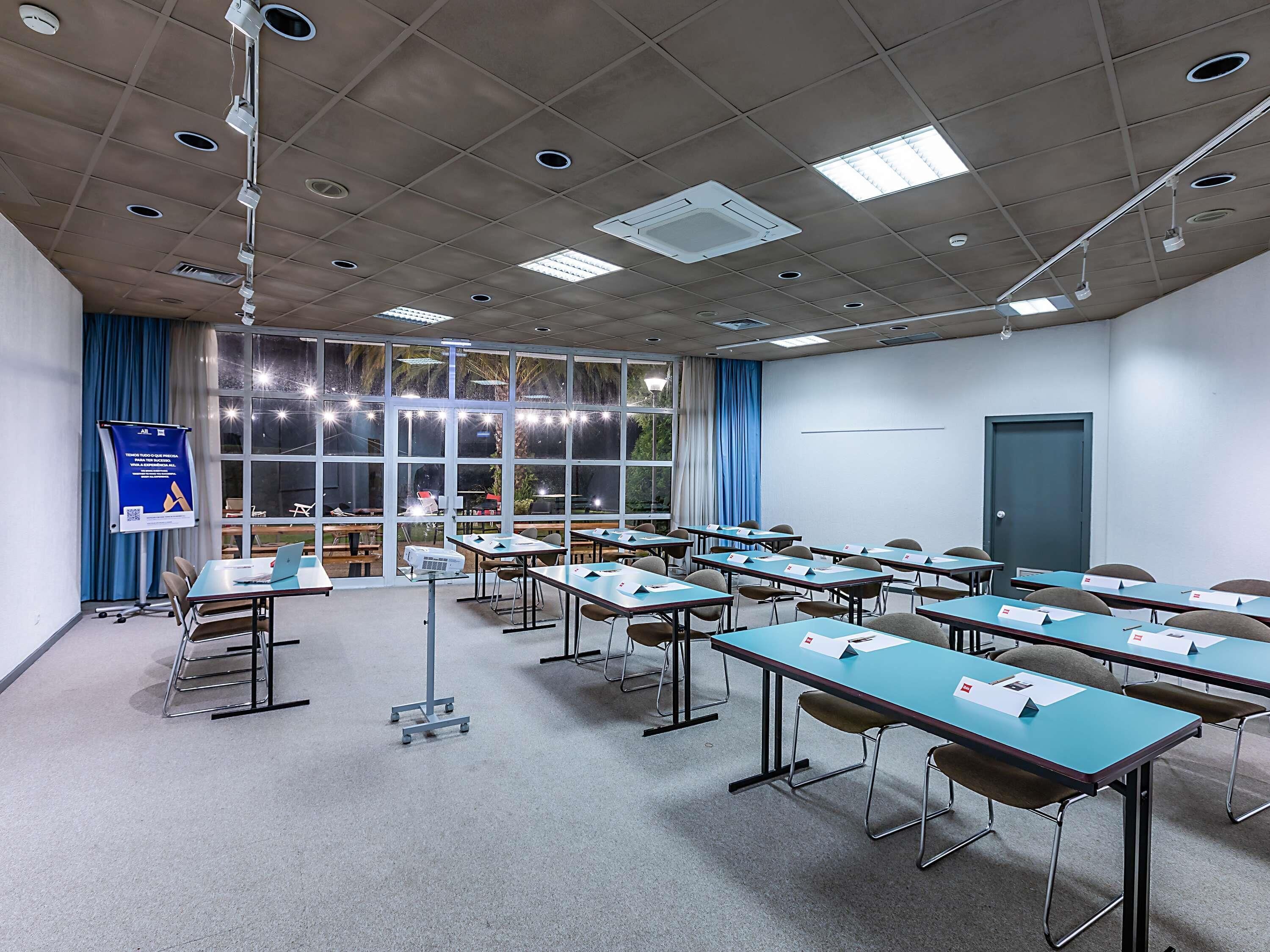 A conference room with tables, chairs, a projector, and a large window with curtains.
