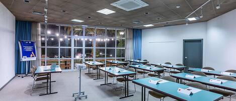 Un salón de conferencias con mesas, sillas, un proyector y un amplio ventanal con cortinas.