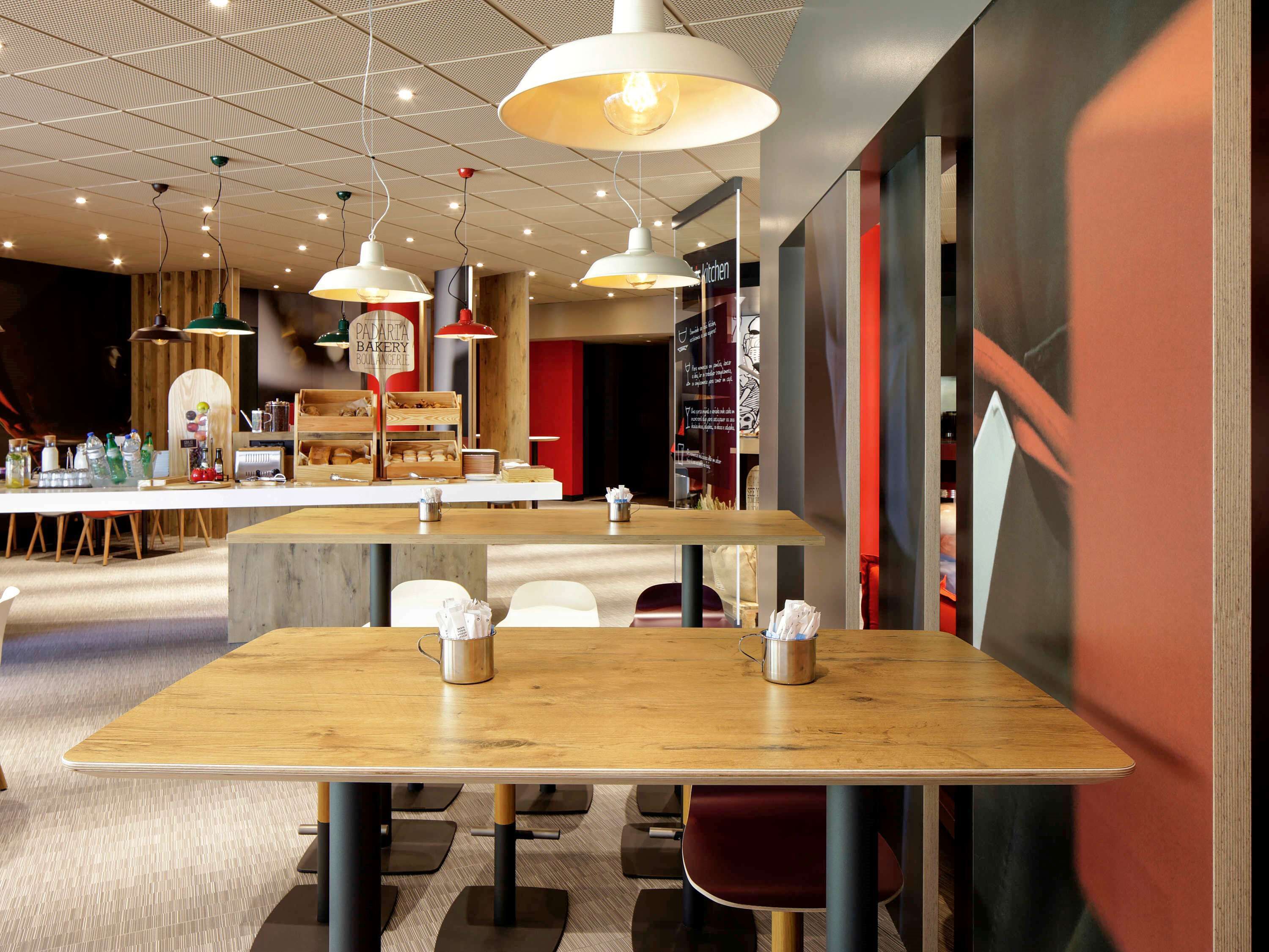 A modern cafe with wooden tables and hanging pendant lights.
