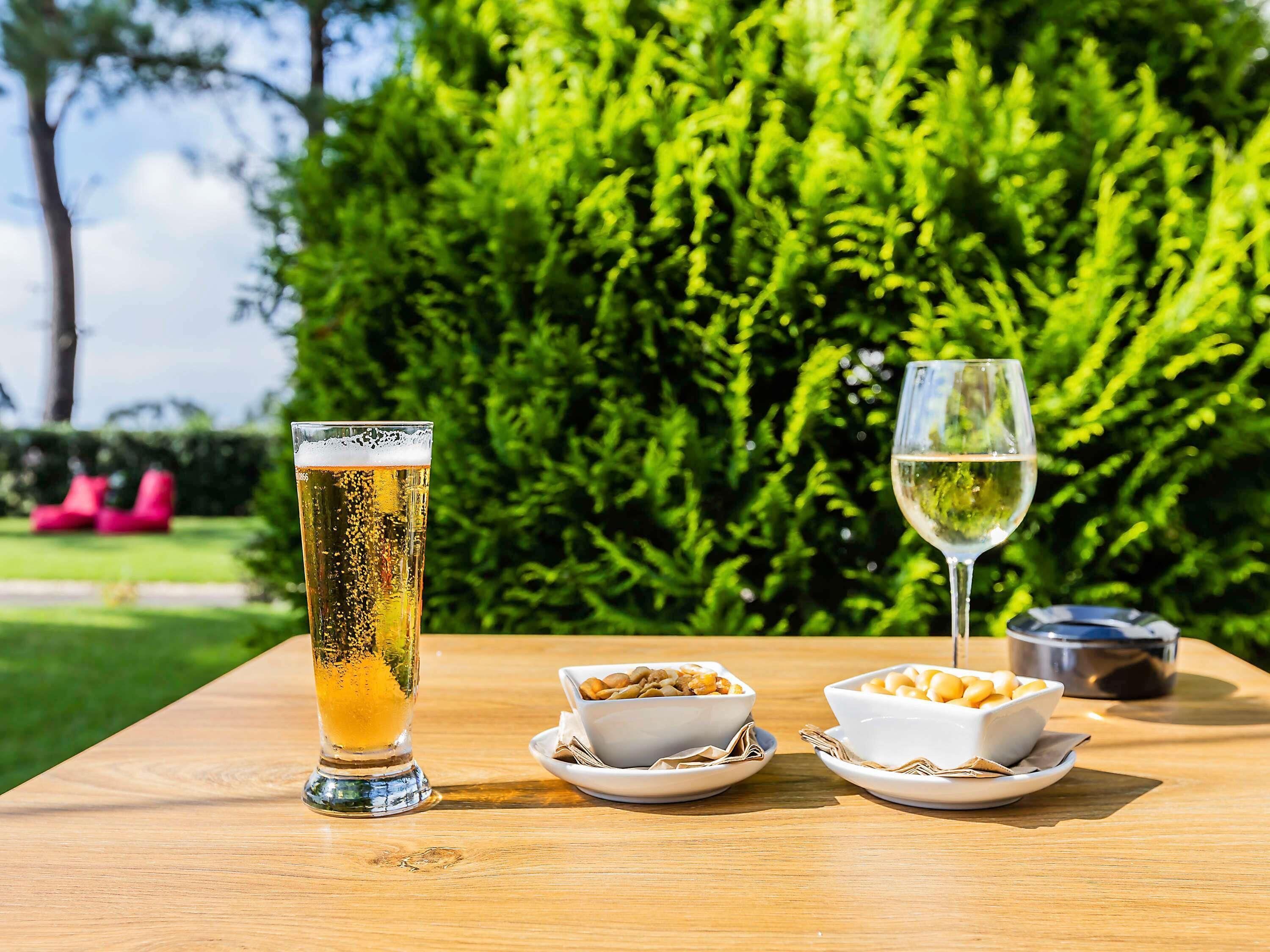 A table with a tall glass of beer, a wine glass, and two bowls of nuts.