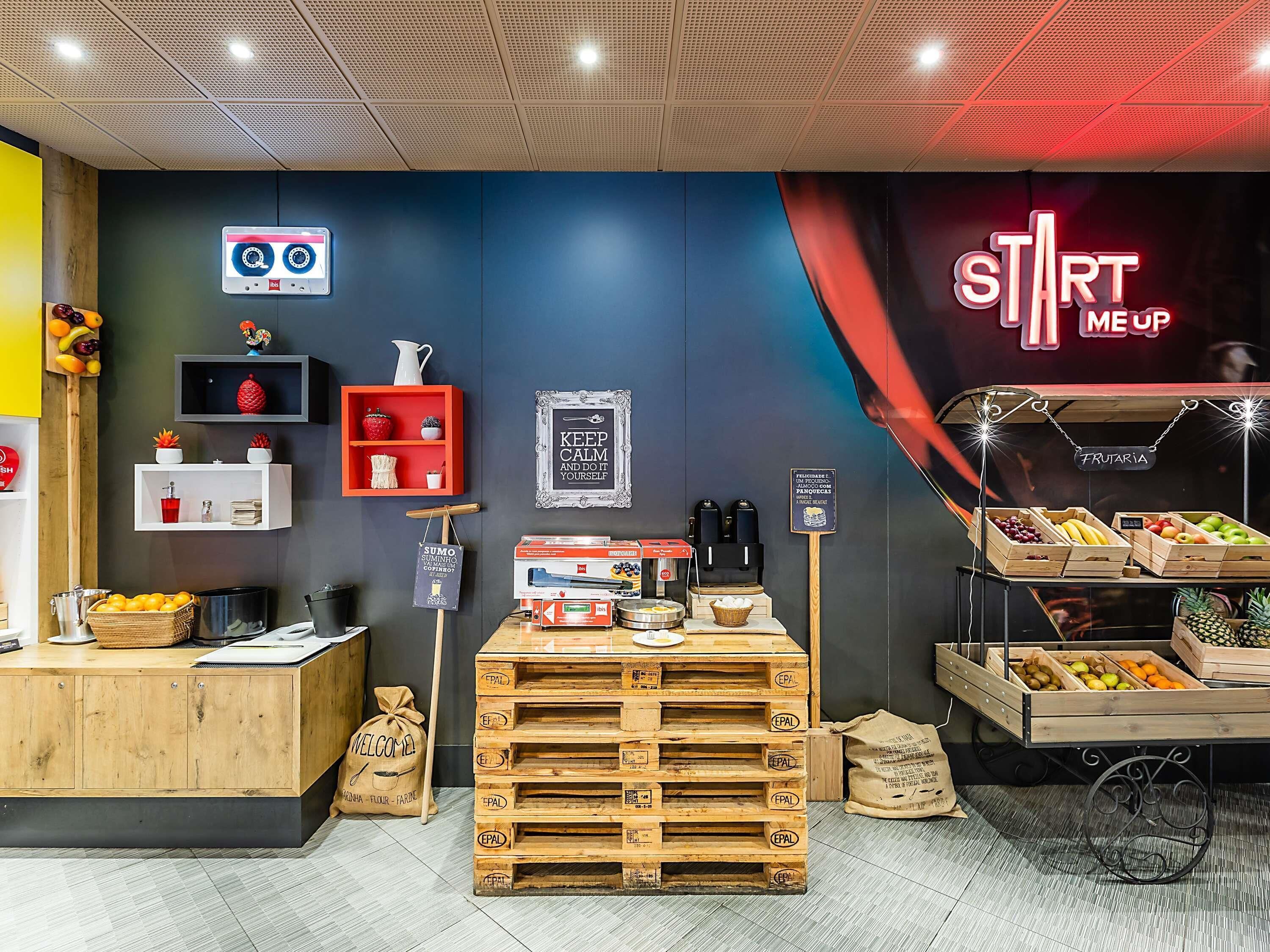 L’intérieur d’un café moderne, avec une machine à café, un présentoir de fruits et une pancarte sur laquelle on peut lire « START ME UP ».