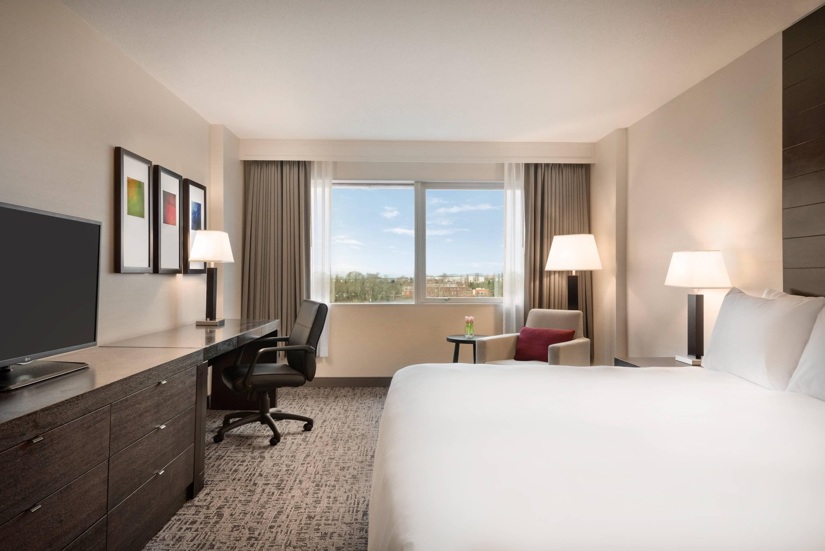 A hotel room with a bed, desk, chair, TV, and a window with a view.