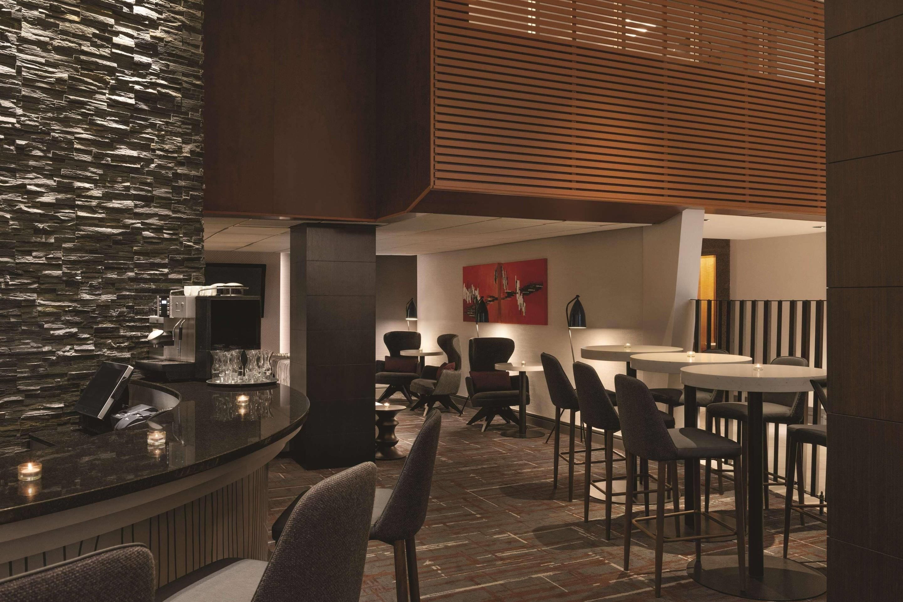 Un área de bar moderna con pared de piedra, listones de madera y mobiliario contemporáneo.