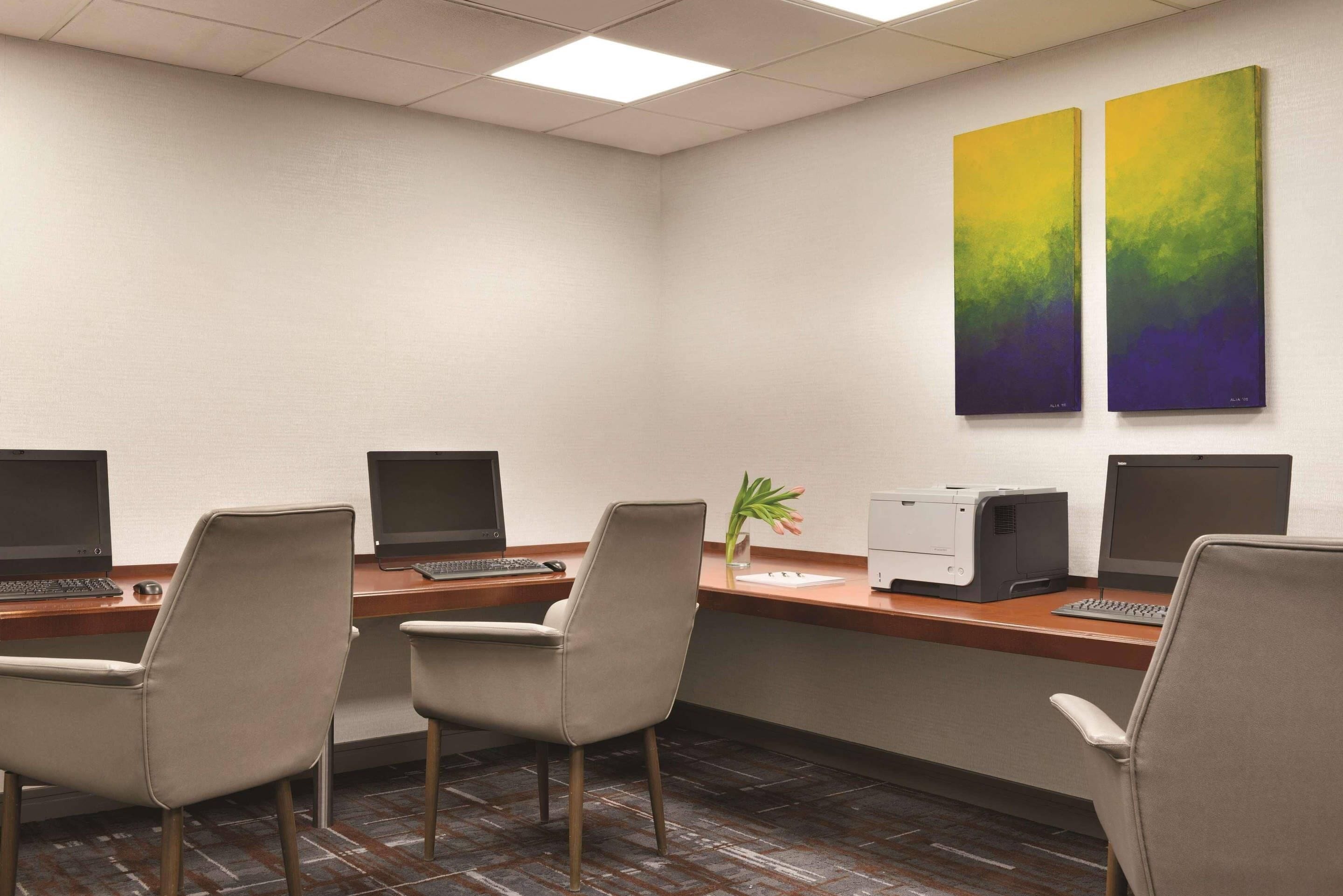 Un salón de conferencias con cuatro escritorios, cada uno con un ordenador y una silla, y dos grandes cuadros abstractos en la pared.