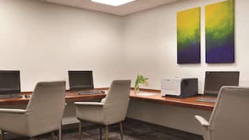 Un salón de conferencias con cuatro escritorios, cada uno con un ordenador y una silla, y dos grandes cuadros abstractos en la pared.
