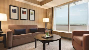 Habitación de hotel con sofá, una mesa de centro con un florero y cuadros en la pared, además de un amplio ventanal con vistas.