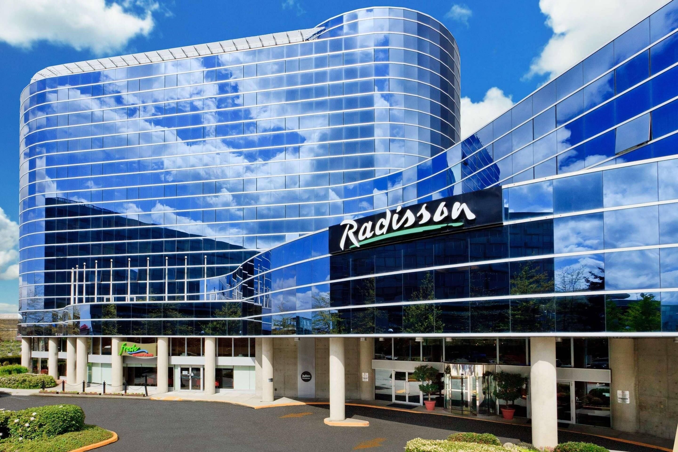 Un hôtel Radisson doté d’une façade moderne en verre, d’une entrée bien visible et d’un espace de stationnement.