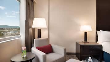 Une chambre d’hôtel avec vue, un canapé, une petite table avec un vase, une table de chevet avec une lampe et un lit.