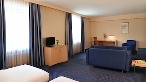 A hotel room with a bed, a desk with a computer, a TV, and a seating area with a couch and chairs.