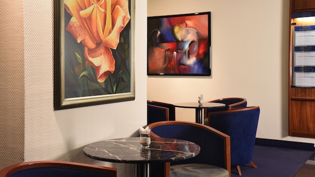 A hotel lobby with a round marble table, blue upholstered chairs, a framed painting of a rose, and a colorful abstract painting on the wall.