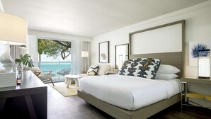 A modern hotel room with a large bed, a desk with a lamp, a chair, and a view of the ocean. - Baker's Cay Resort Key Largo, Curio Collection by Hilton (Key Largo)