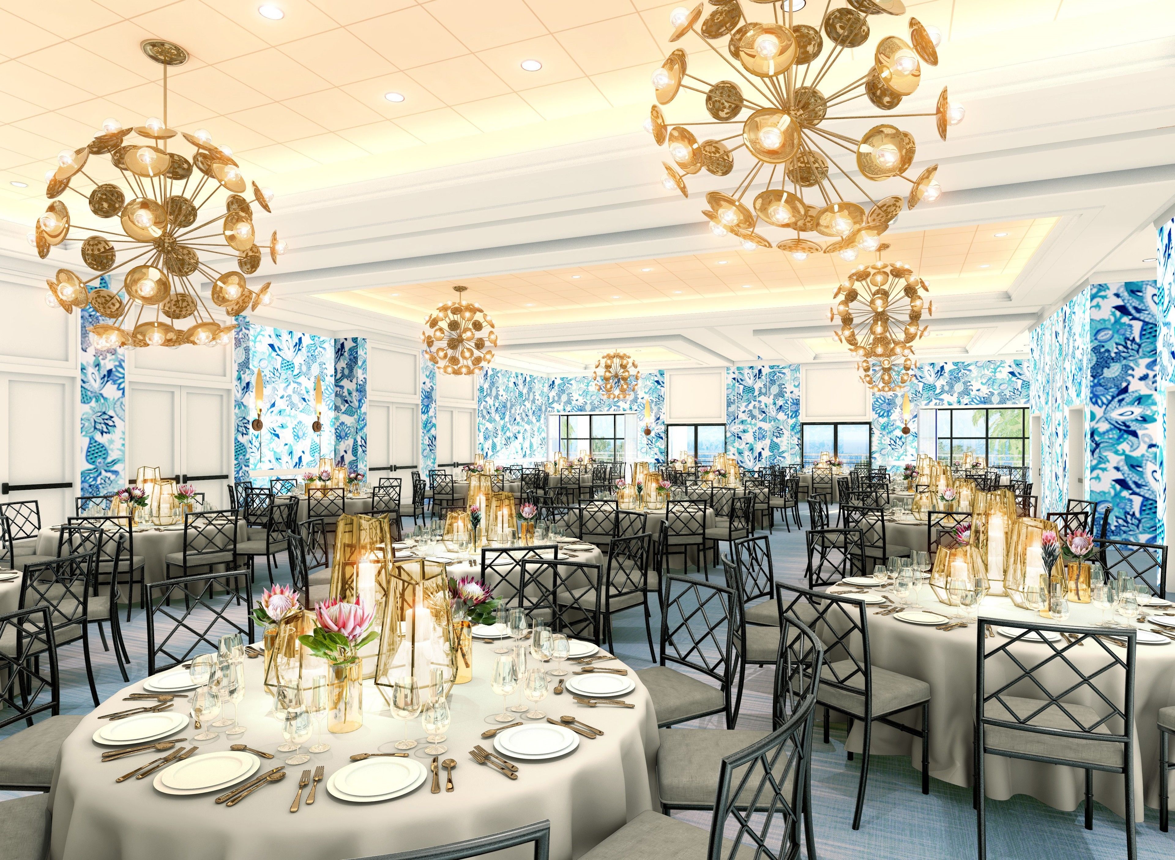 A banquet hall with round tables, gold chandeliers, and blue floral wallpaper.