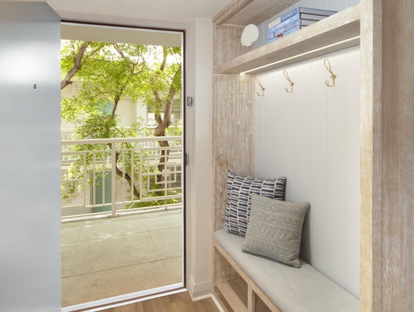 Ein Zimmer mit einer Schiebetür und einem Balkon, eine Bank mit Kissen, ein Holzregal mit Büchern und einem Wandhaken.