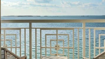A balcony with two wicker chairs and a small table, overlooking a calm sea and distant islands.