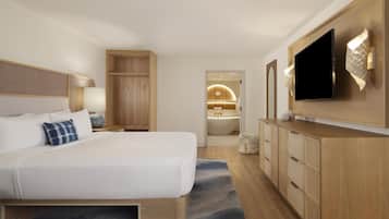 Et moderne hotelværelse med en stor seng, et fjernsyn, træskabe og et badeværelse, der kan anes gennem en åben dør.