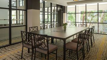 A conference room with a large table, chairs, and large windows offering a view of trees.