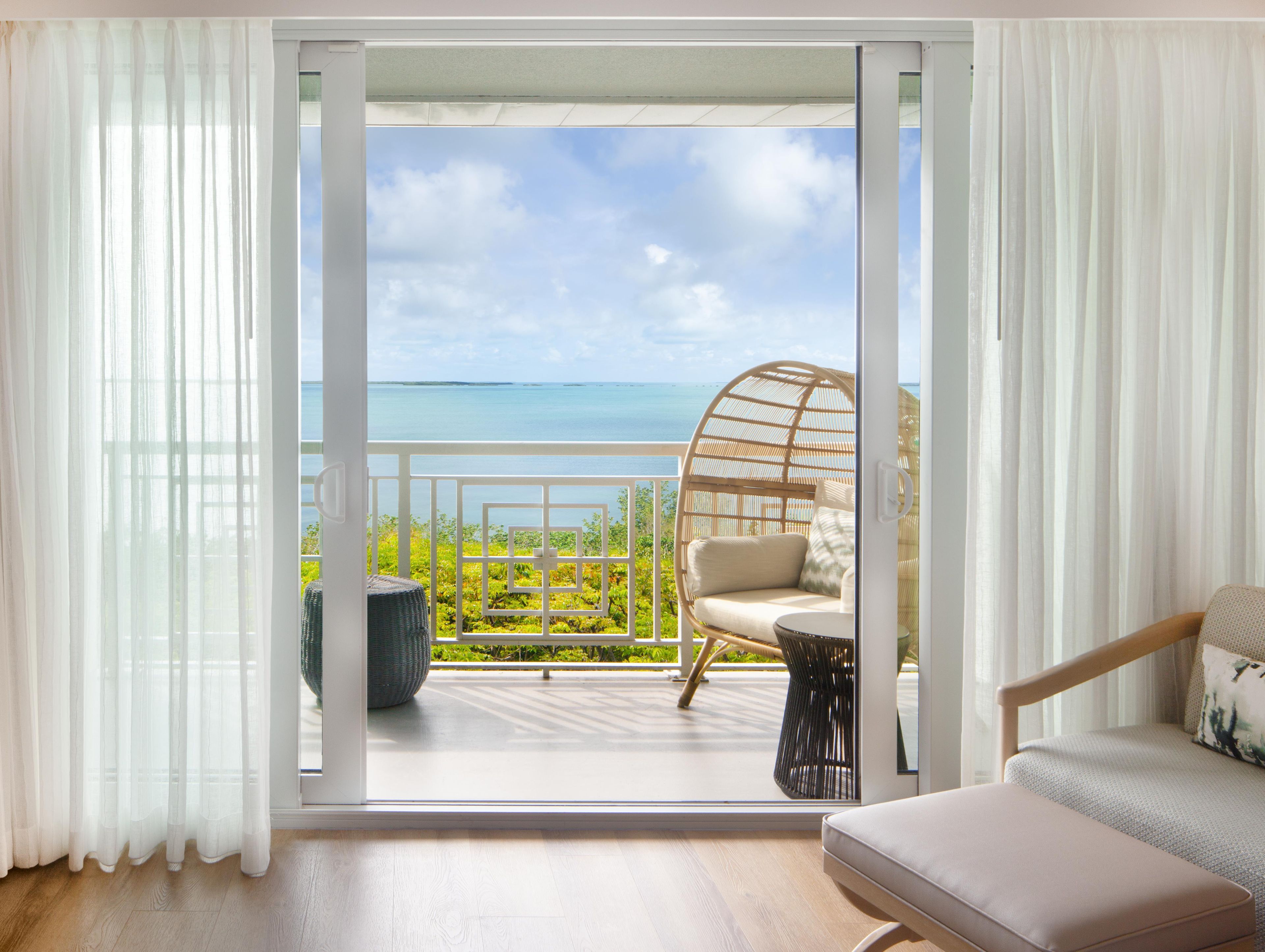 Una habitación con balcón, una silla de mimbre, un banco de madera y vista al mar.