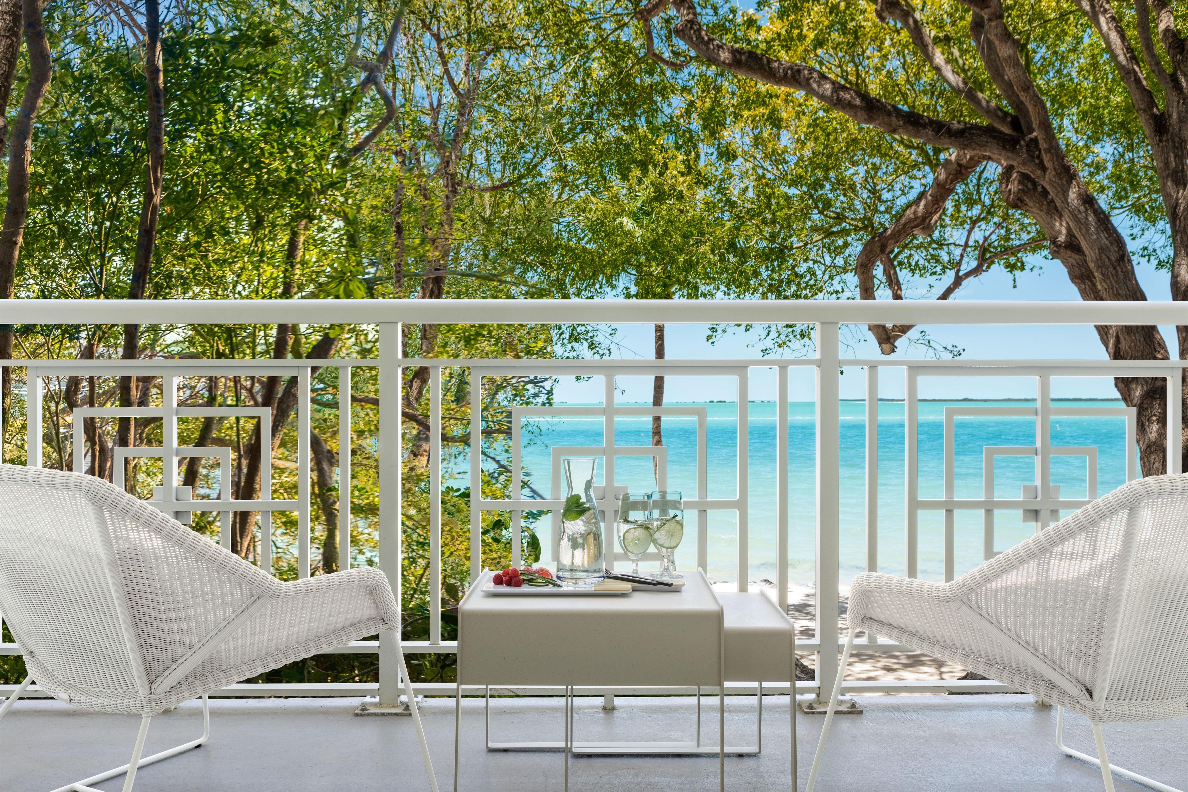 A balcony with white wicker furniture, a table, and a view of the sea.