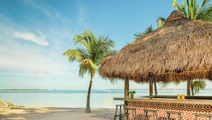 A beach bar with a thatched roof, palm trees, and a view of the sea.