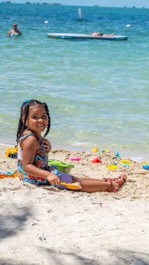 A child sitting on a beach with sand toys and a green bucket nearby.