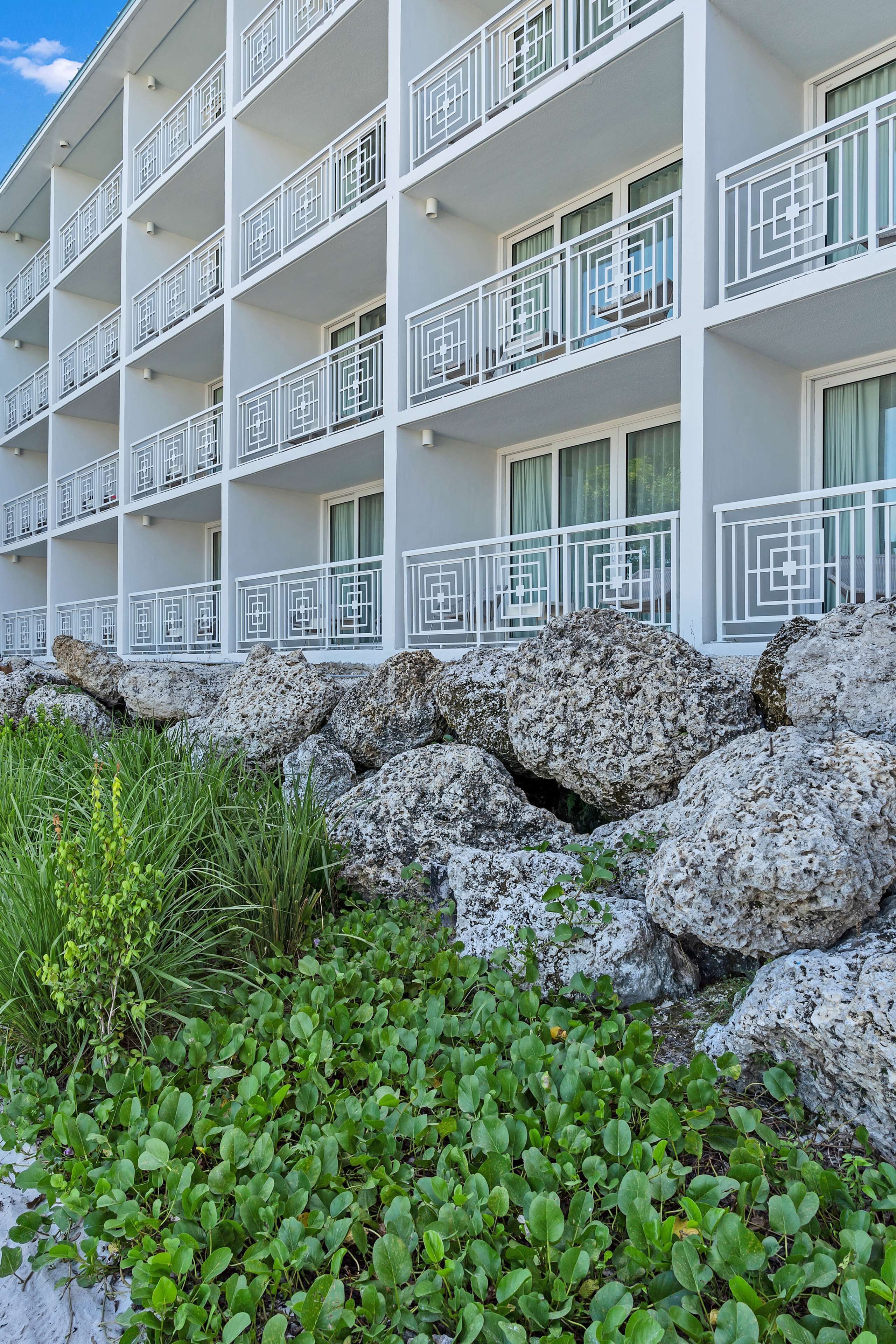 Un hotel de varios pisos con balcones, un jardín rocoso y plantas verdes.